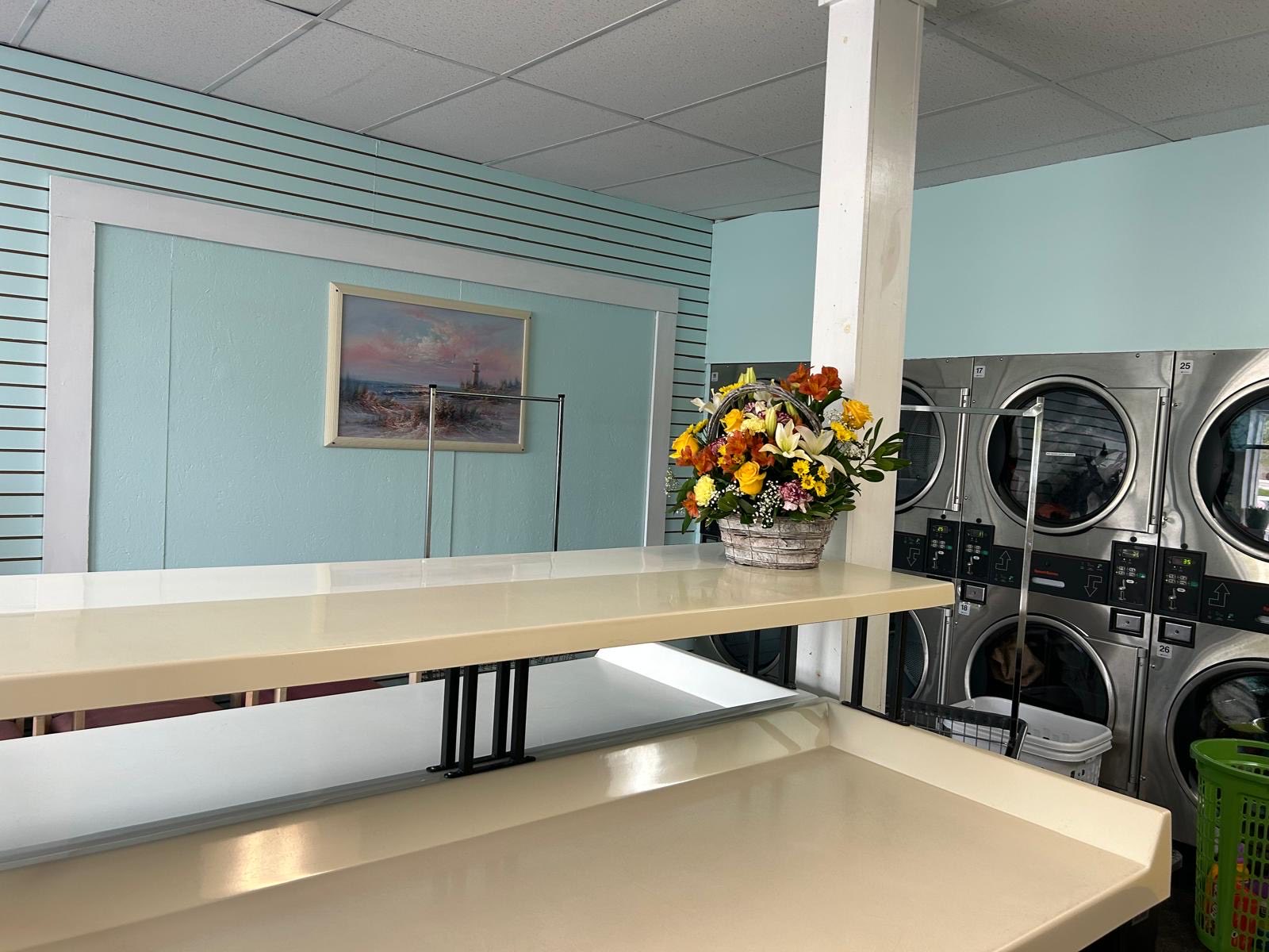 Folding counters and stacked dryers inside Bayside Coin Laundry, where wash and fold orders are prepared